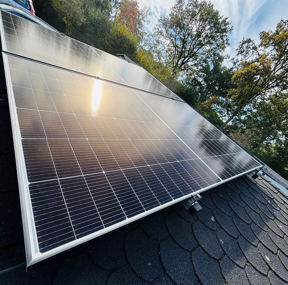 Fertig montierte Solarmodule auf dem Gartenhausdach, in denen sich die Sonne spiegelt