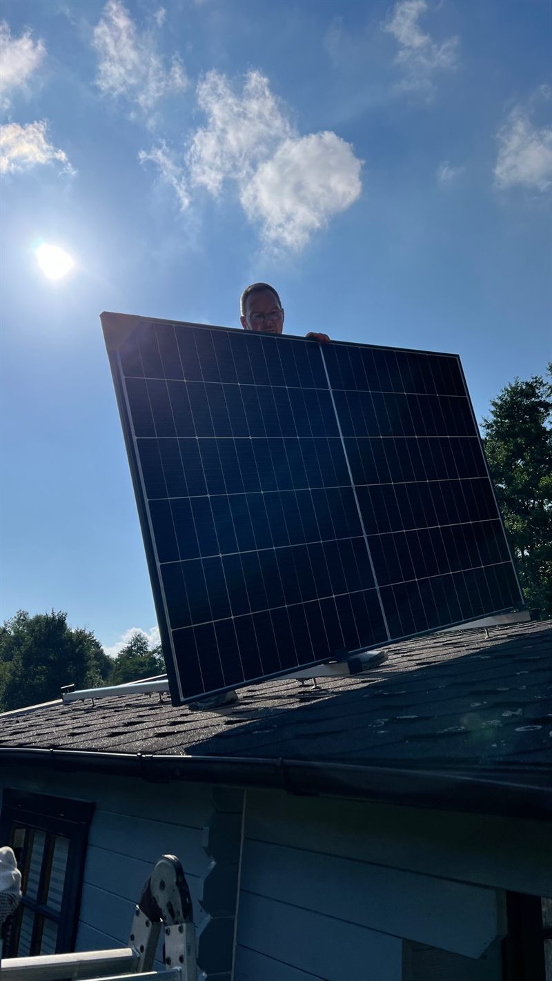 Sascha Meuser hebt ein Solarmodul auf das Gartenhausdach, im Hintergrund die Sonne